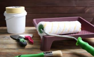 Paint roller in tray and tools on wooden table