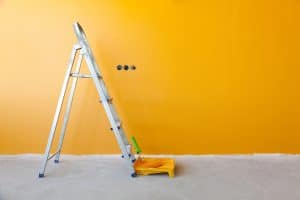 ladder, paint can and paint roller in a bright yellow wall