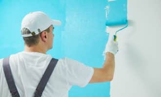 Painter worker with roller painting wall surface into color at home impovement and refurbishment